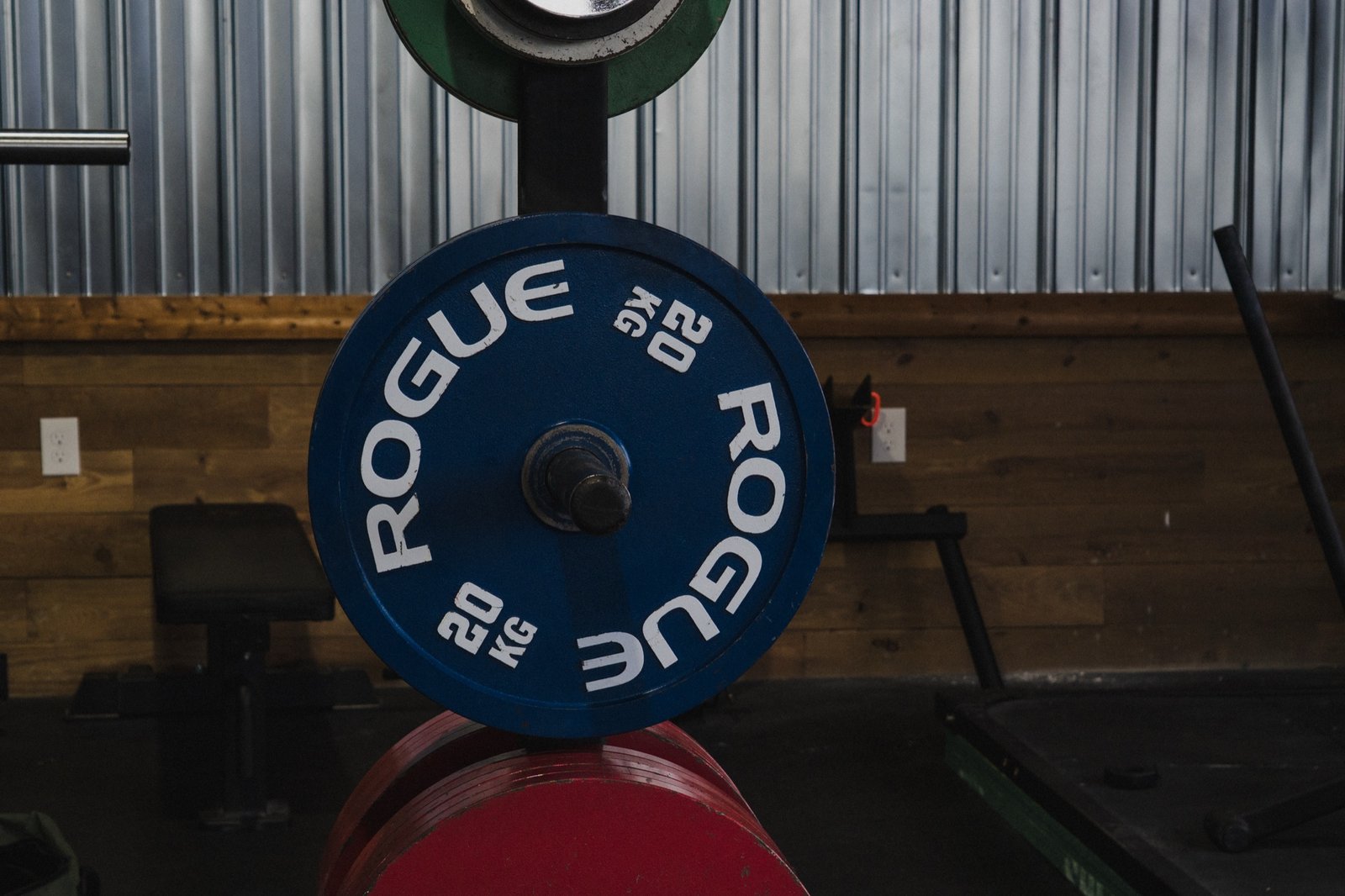 Close detail of a blue Rogue 20kg competition plate racked against The Den's corrugated steel and reclaimed wood wall.