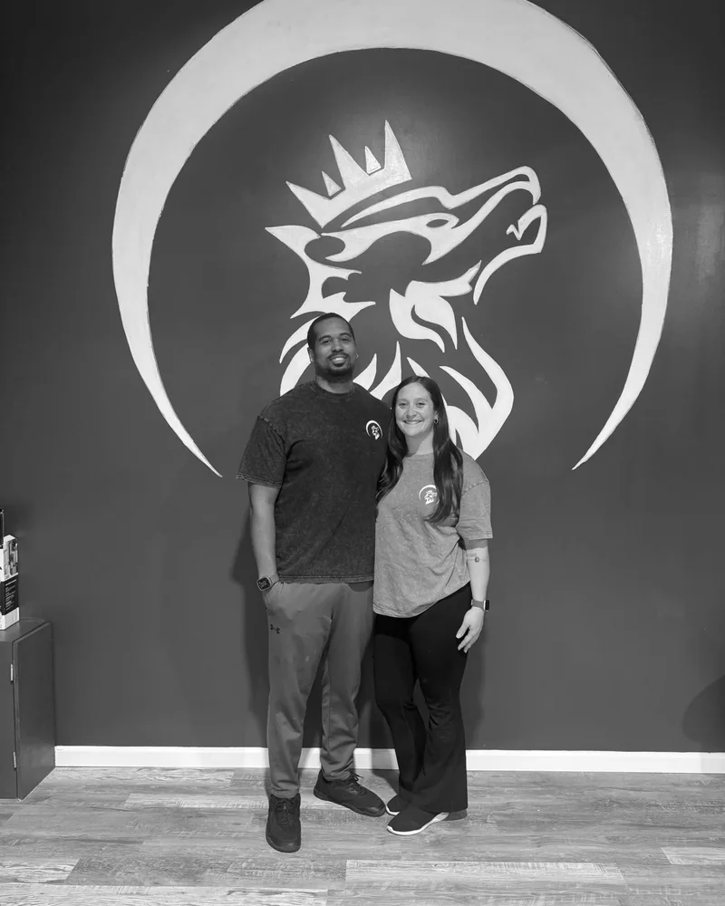 Eric and Keara Thompson standing together in front of the hand-painted wolf mural at Wolf Dynasty Fitness.
